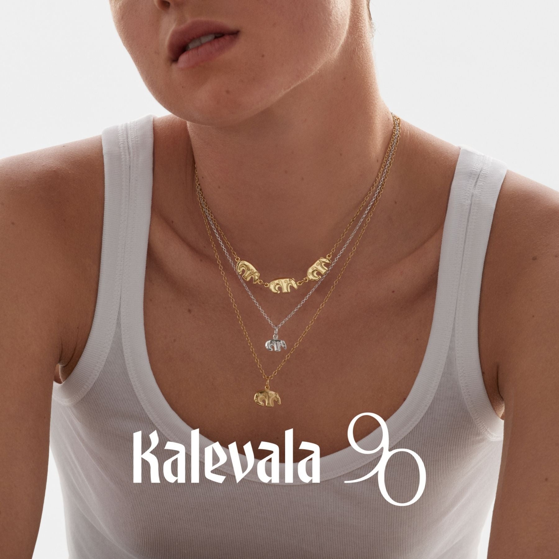 Kalevalan pronssinen kaulakoru, jossa kolme pientä karhuhahmoa rinnakkain naisen kaulalla valkoisen topin yllä