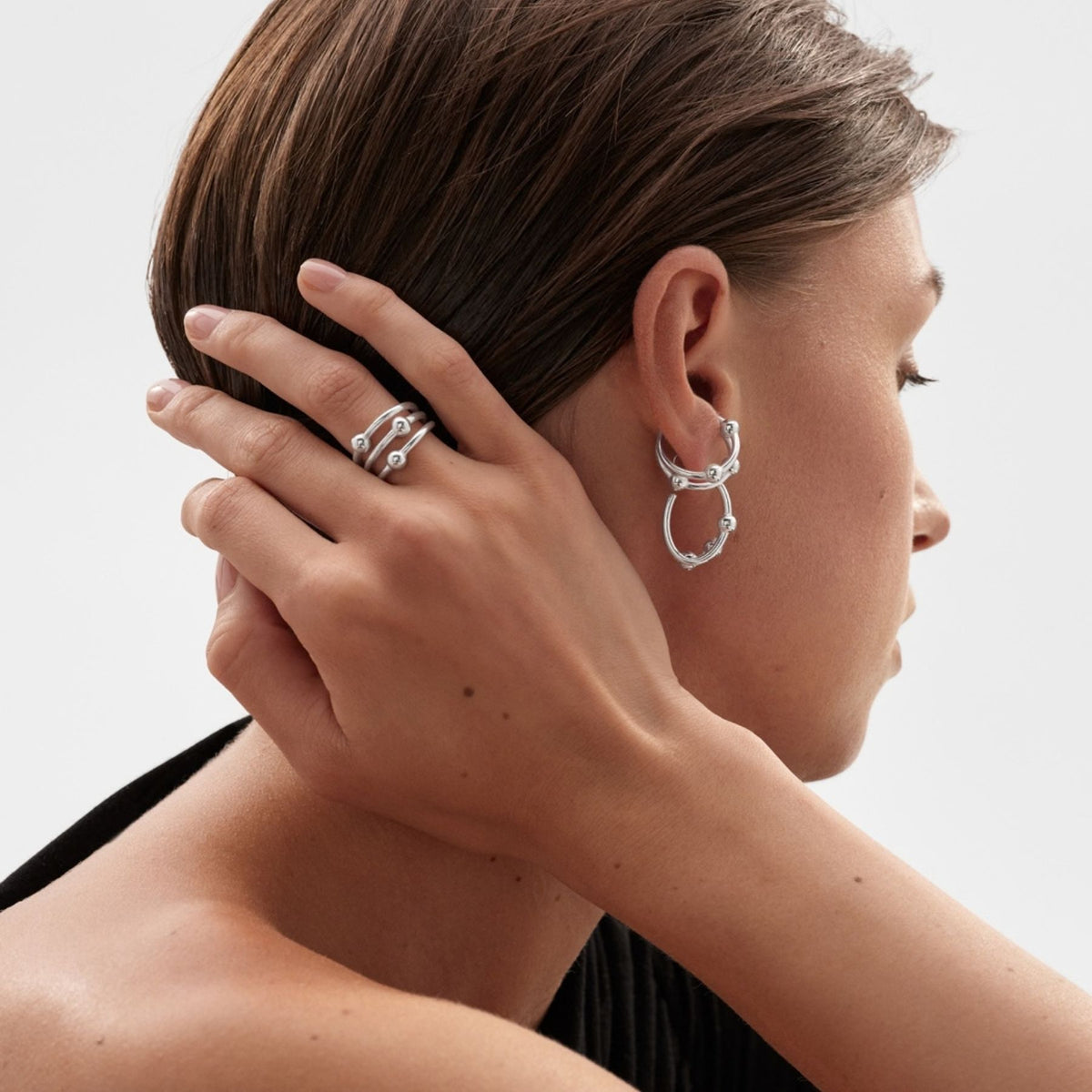 Kalevalan hopeinen ear cuff korvakoru naisen korvassa, sivuprofiilissa käsi hiuksilla ja hopeiset korurenkaat näkyvissä