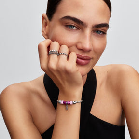 Pandora Moments hopeisessa rannekorussa näkyy pieni pinkki hymynaamahela ja muita heloja mallin ranteessa