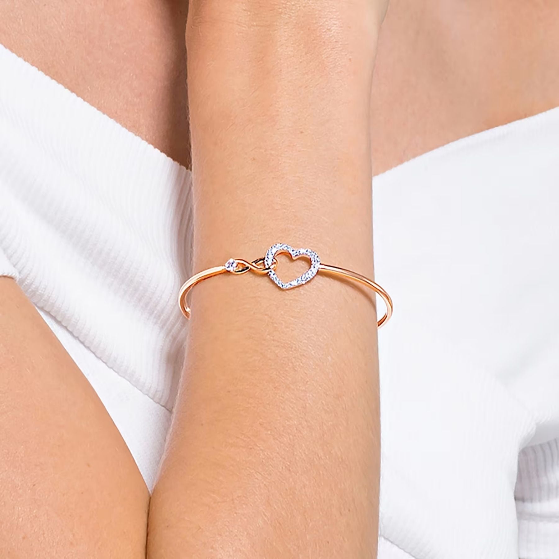 Swarovski rosekultainen kristallirannekoru, jossa säihkyvä infinity-symboli ja sydänrannekoru ranteessa